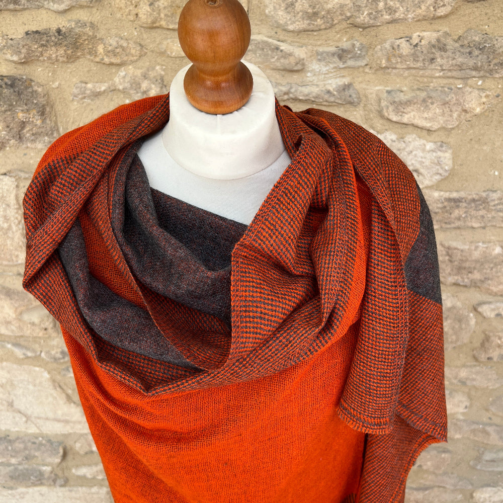 Mannequin wearing a grey/brown and orange patterned cashmere scarf against a stone wall background