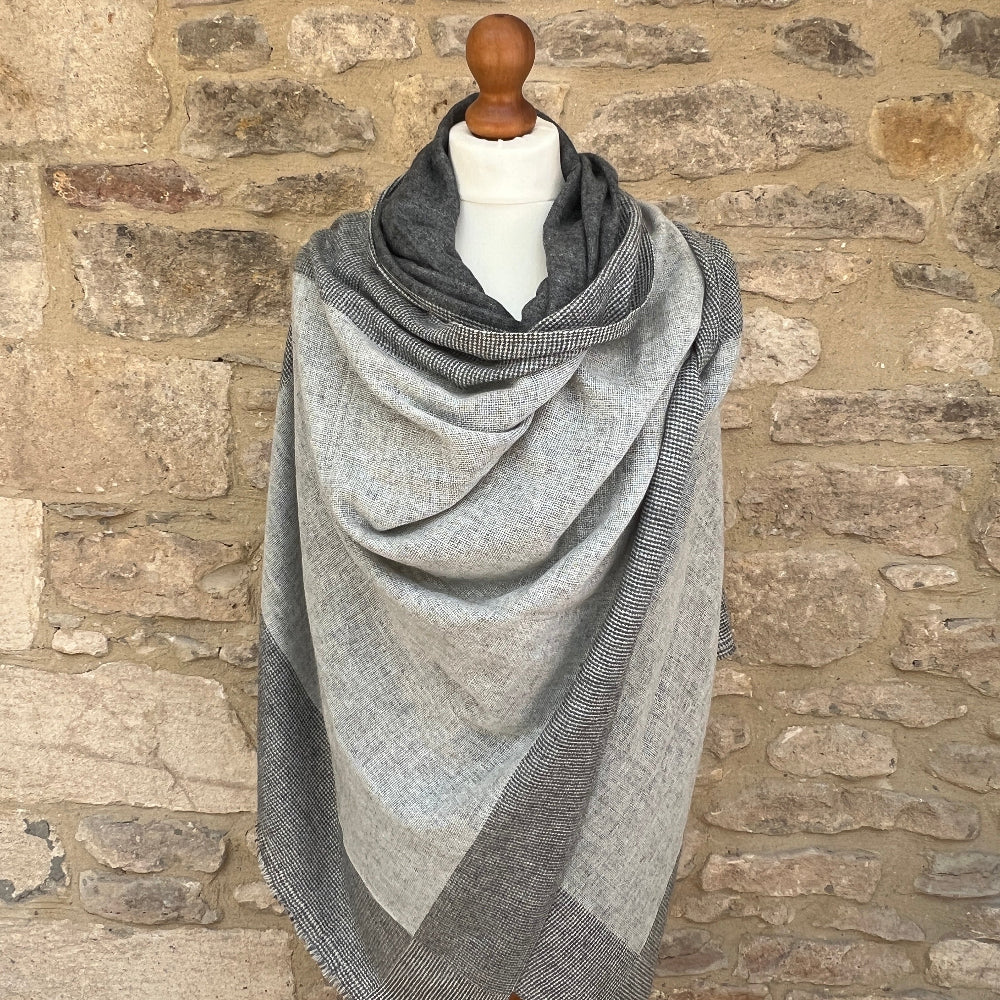 Gray plaid scarf on a mannequin against a stone wall background