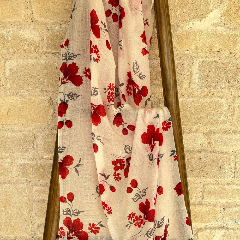 Floral cashmere scarf with red flowers on a wooden stand against a beige brick wall.