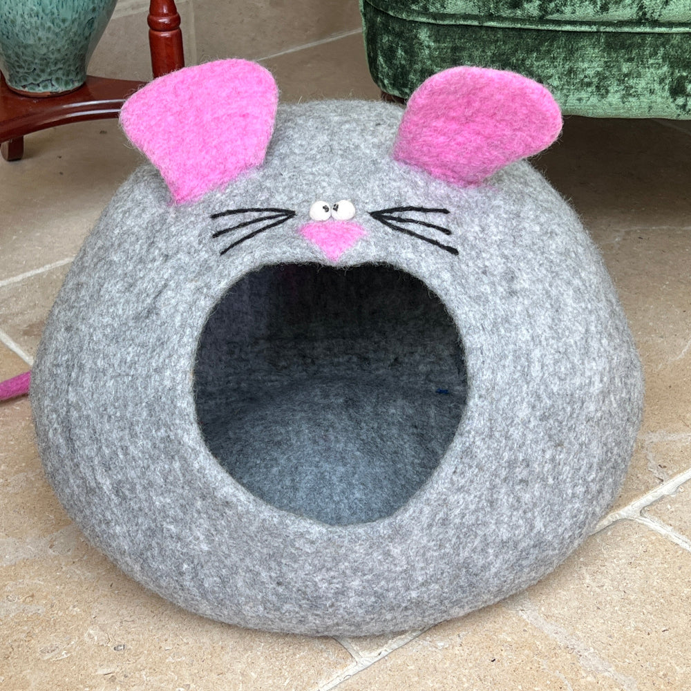 Gray 'Mouse' cat bed with pink ears and black whiskers in front of a green velvet armchair.