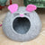 Gray 'Mouse' cat bed with pink ears and black whiskers in front of a green velvet armchair.