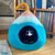 Green velvet armchair with a patterned pillow next to a blue and pink pet bed in a room with a stone wall.