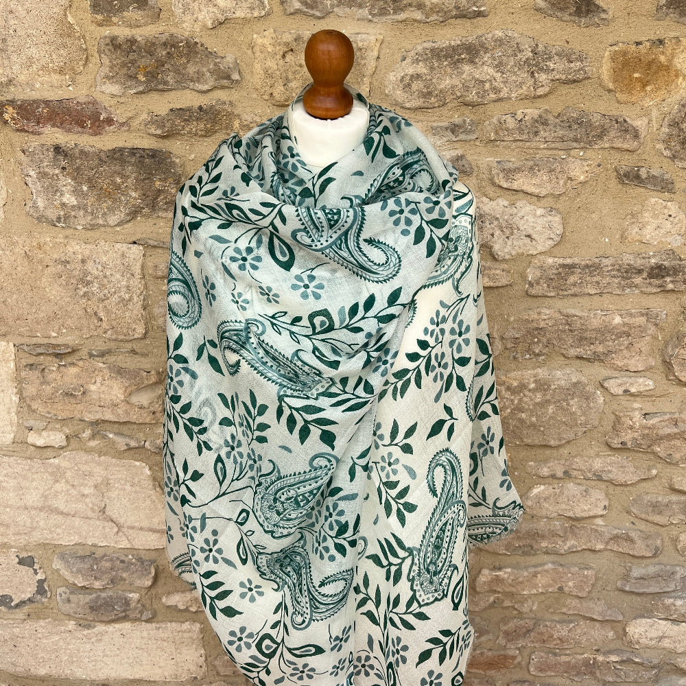 Cashnere pashmina scarf with green paisley leaf pattern draped over a mannequin against a stone wall.