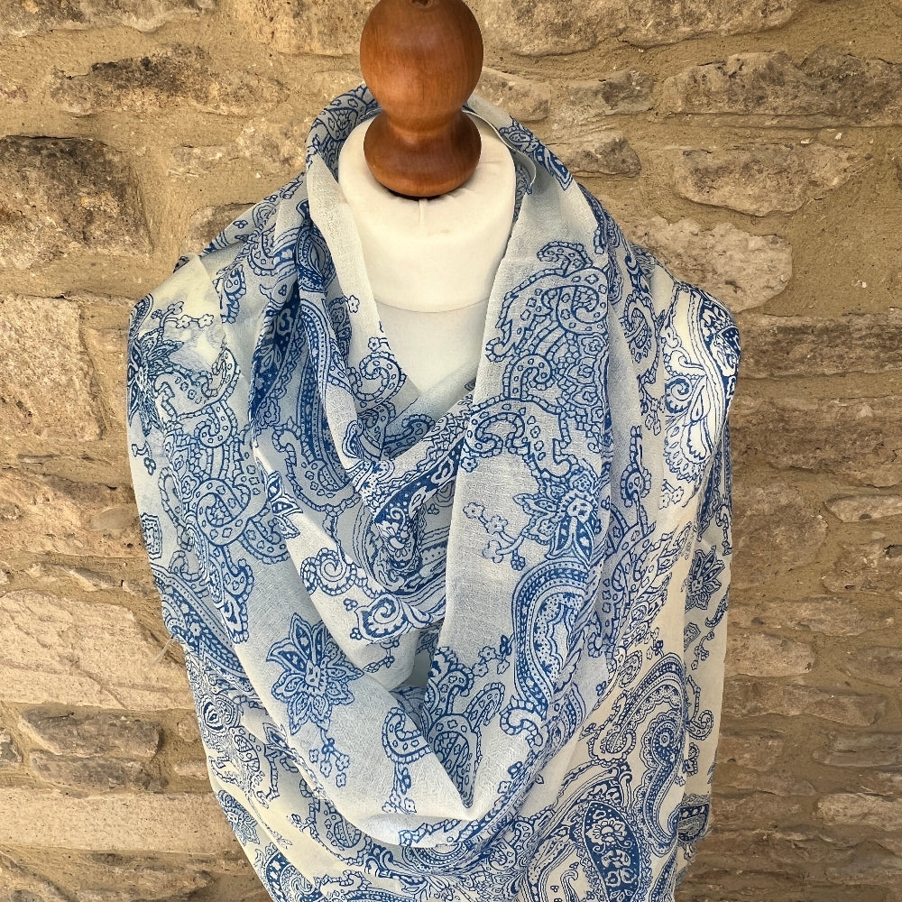 Mannequin wearing a blue and white paisley patterned cashmere pashmina scarf against a stone wall.