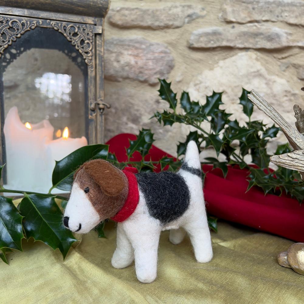 Meet &#39;Patch&#39;, a charming felted wool dog that brings artisanal character to any space.

This companion features a distinctive patchwork design with rich brown tones, complemented by a striking crimson scarf. Meticulously hand-stitched from premium wool, each piece showcases the craftsmanship of its maker.

Shown on gold silk fabric with candles, festive holly, decorative accents against a cotswold stone wall. 
