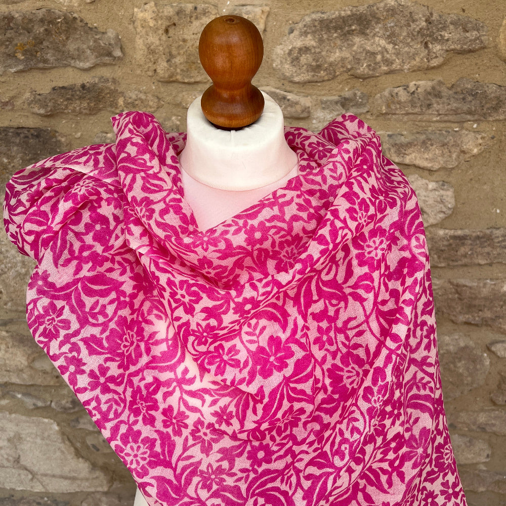 Pink floral patterned  cashmere scarf on a mannequin against a stone wall background