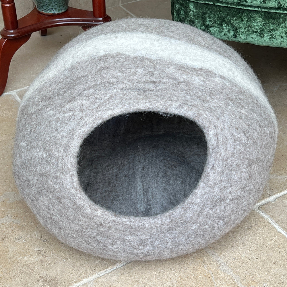 Green velvet armchair with a patterned cushion and a light brown andn cream striped pet bed on a tiled floor.