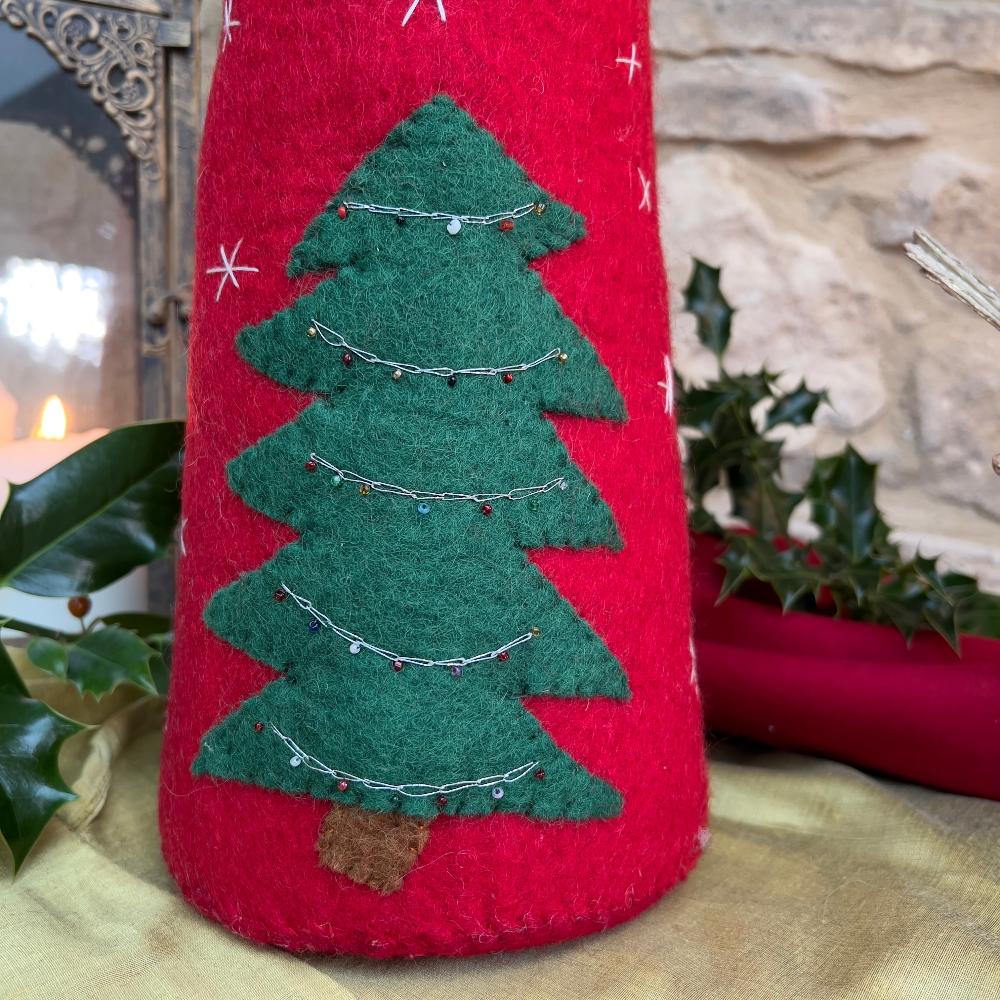 Bring festive charm to your home with this exquisite artisan handcrafted Father Christmas figure.

Meticulously created from premium felted wool, it showcases a luxuriously soft faux fur beard and intricate hand-stitched snowflake embellishments adorning the hat and body. The design features charming holly and berry appliqués on the hat, while the back displays an ornate Christmas tree decorated with sparkling beads. Shown on gold silk fabric with holly and festive candle and decorative items. 