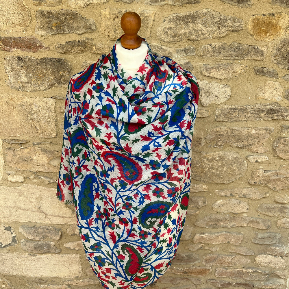 Red green and blue patterned gossamer cashmere pashmina on a mannequin against a stone wall background. 