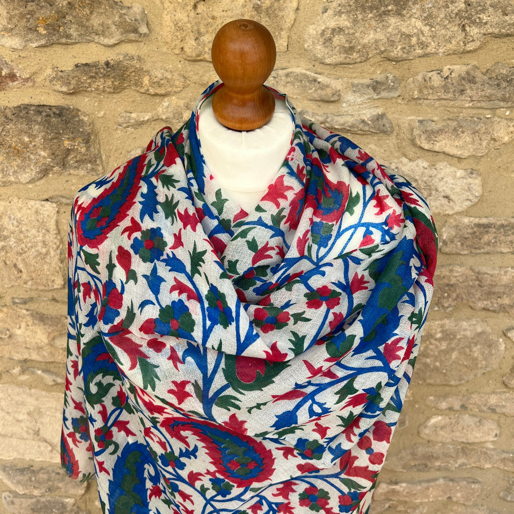 Red green and blue patterned gossamer cashmere pashmina on a mannequin against a stone wall background. 