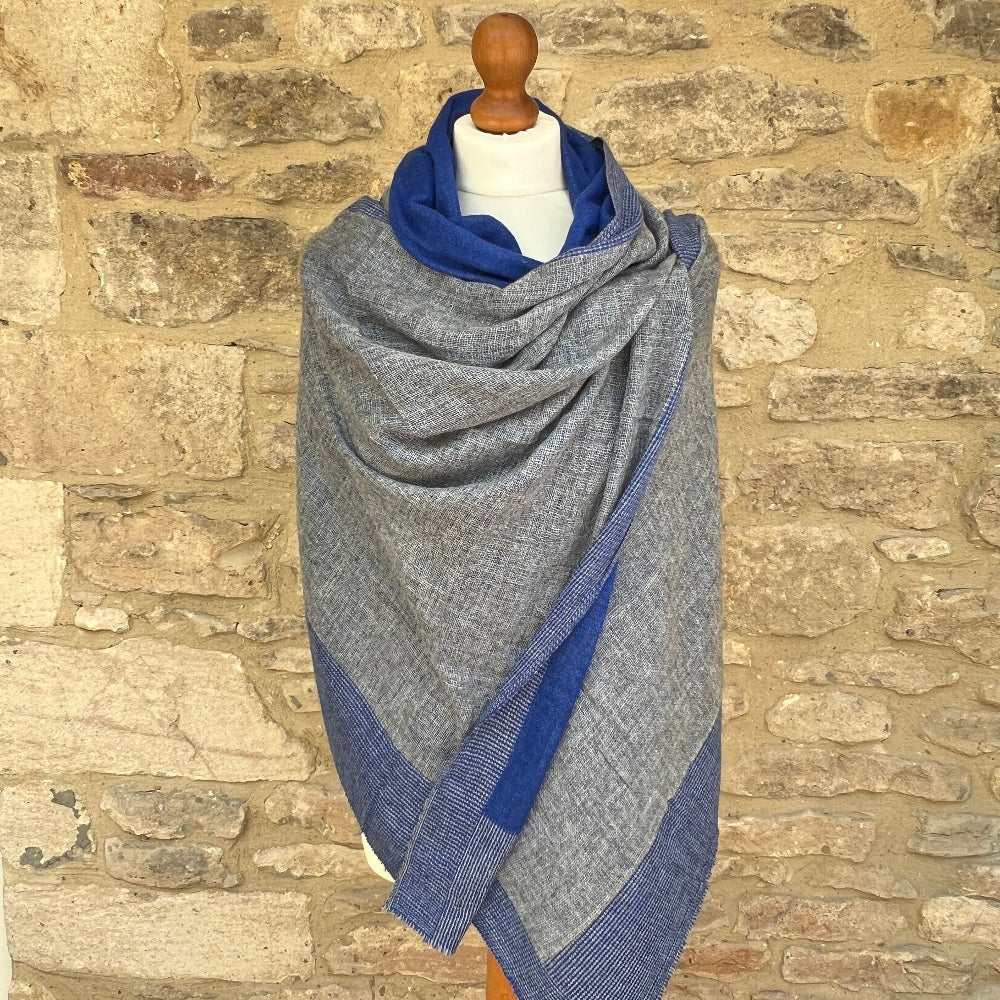 Reversible grey and blue cashmere pashmina on a mannequin against a cotswold stone wall.