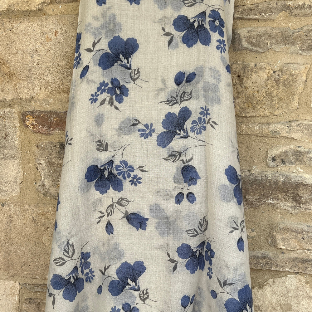 Floral-patterned gossamer chasmere pashmina scarf  with blue flowers on a white background against a brick wall.
