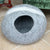 Gray pet bed  with a white stripe in front of a green velvet armchair with decorative pillows.