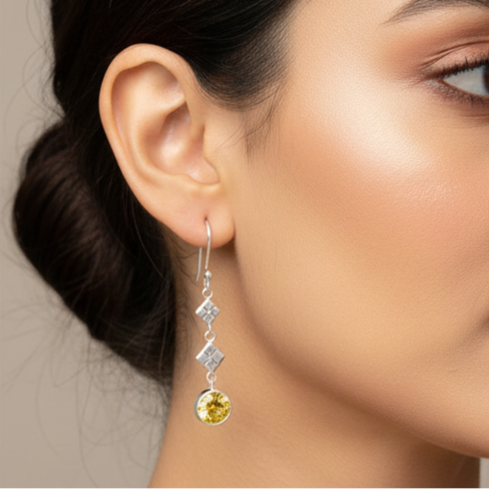 Yellow Topaz &amp; Silver Drop Earrings against a cream wall background hanging from a branch with green leaves. 