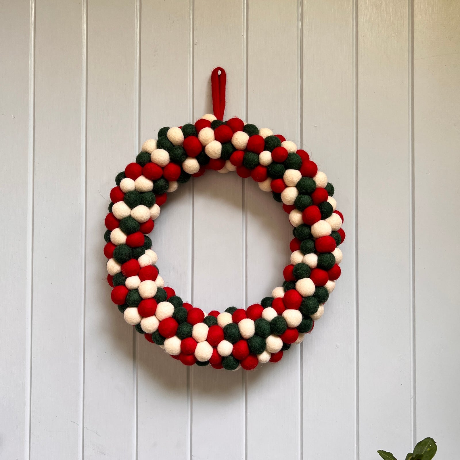 Handcrafted Felted Wool wreath with Red, White & Green colour decoration. A Seasonal Wreath against a stone wall with Christmas decorations and candles.