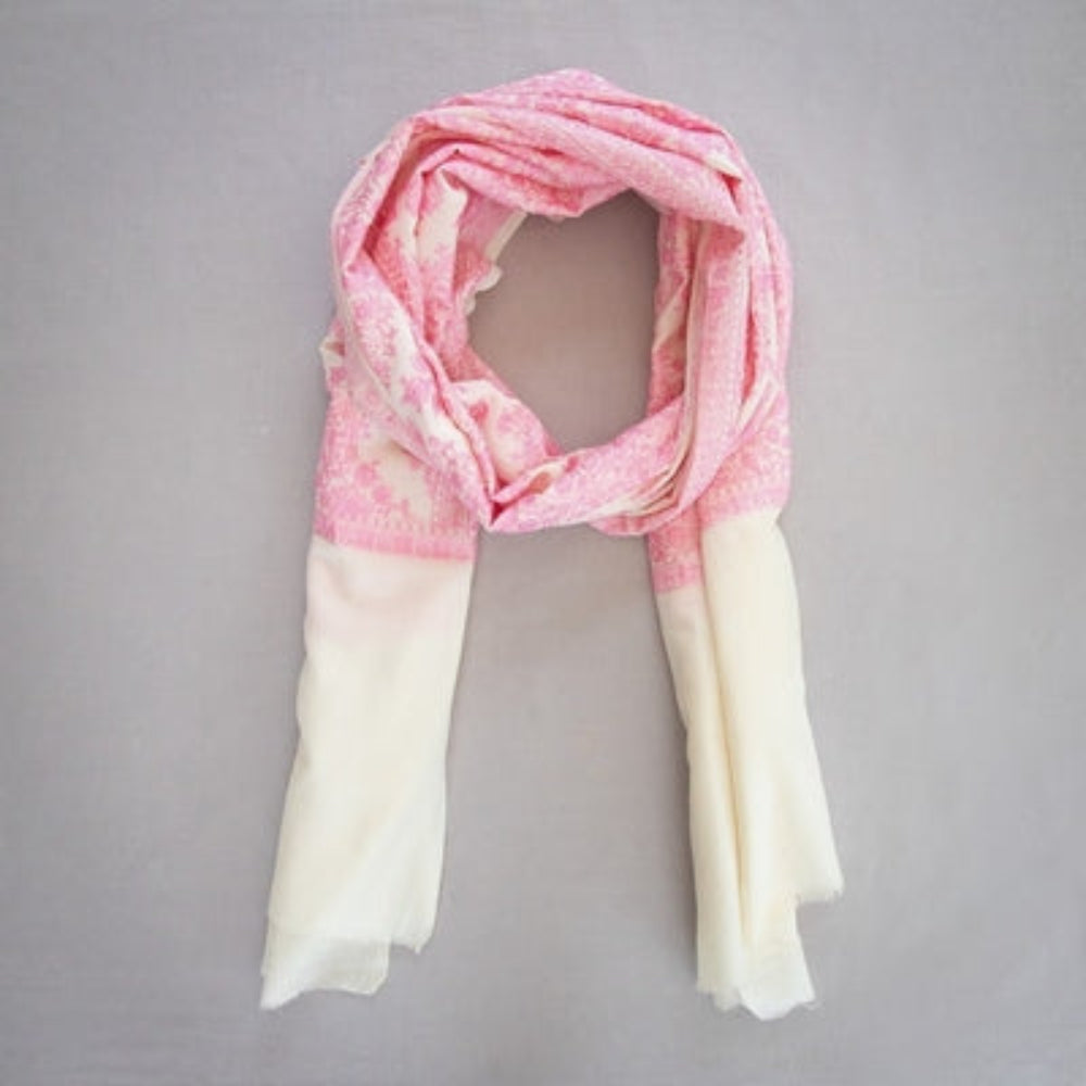 A cream and pink embroidered cashmere pashmina hanging on a branch of a tree with a green background.