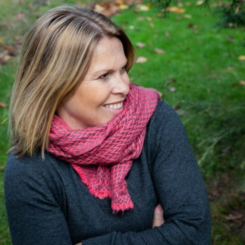 Douée -  Wool & Cashmere Scarf in a Salmon herringbone weave shown on a female model with blonde hair against a green grass background. 