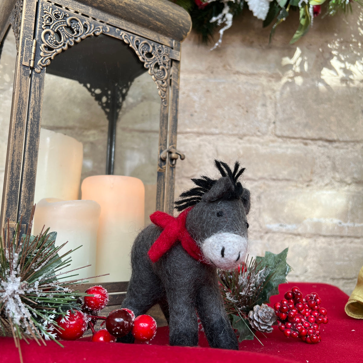 Discover the charm of our artisan, handcrafted felted wool Donkey.&amp;nbsp;

A delightful festive companion perfect for adding warmth to your seasonal décor. Each piece is handcrafted crafted from pure felted wool with hand-stitched details and dressed in a vibrant red scarf that captures the spirit of the season.

Shown against a cotswold stone wall background on gold silk fabric with festive holly and candles and decorative accents. 