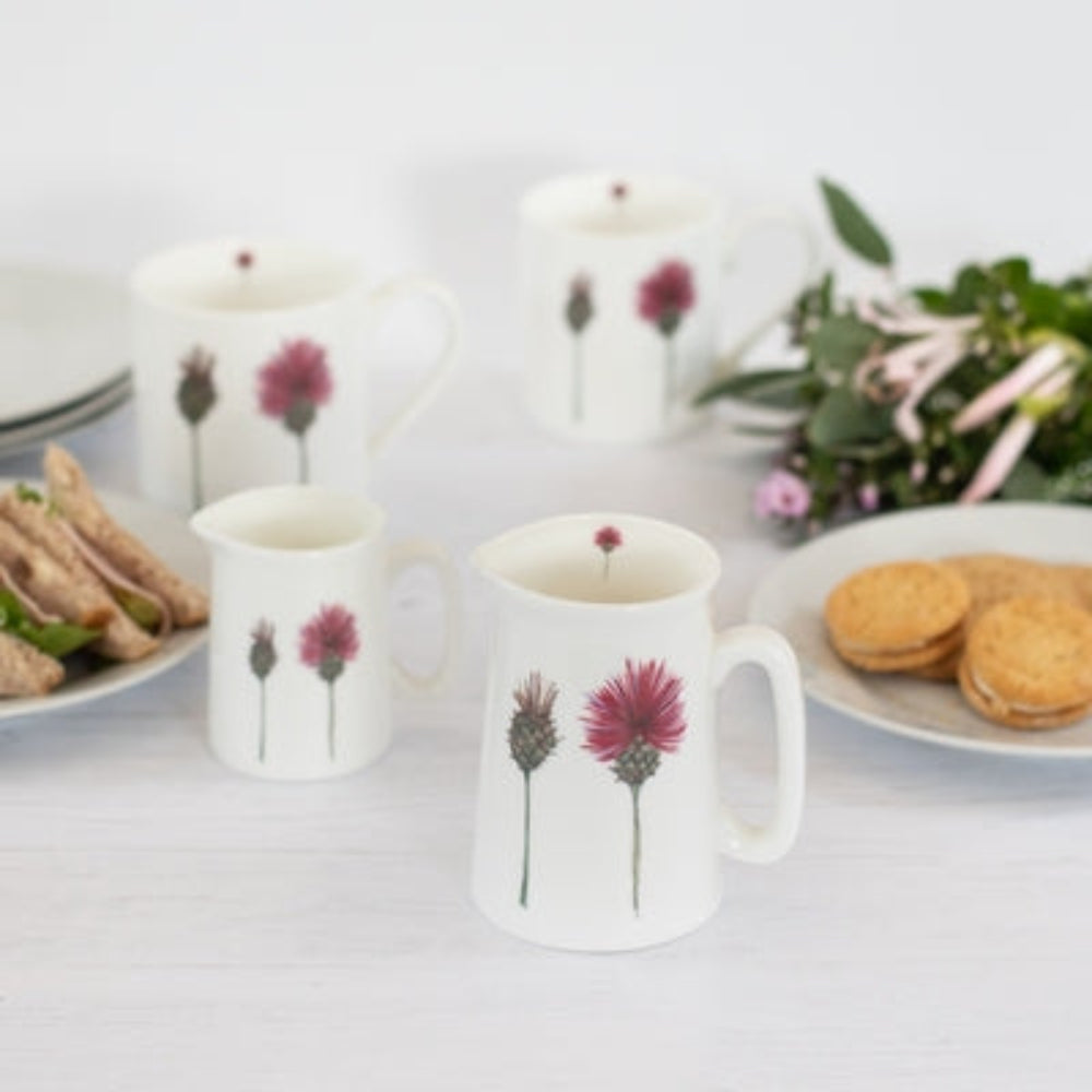 Douée -  Bone China Jug - Thistles shown on a white table with sandwiches and biscuits and fresh flowers against a white background. 