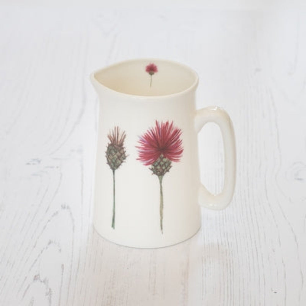 Douée -  Bone China Jug - Thistles shown on a white table with sandwiches and biscuits and fresh flowers against a white background. 