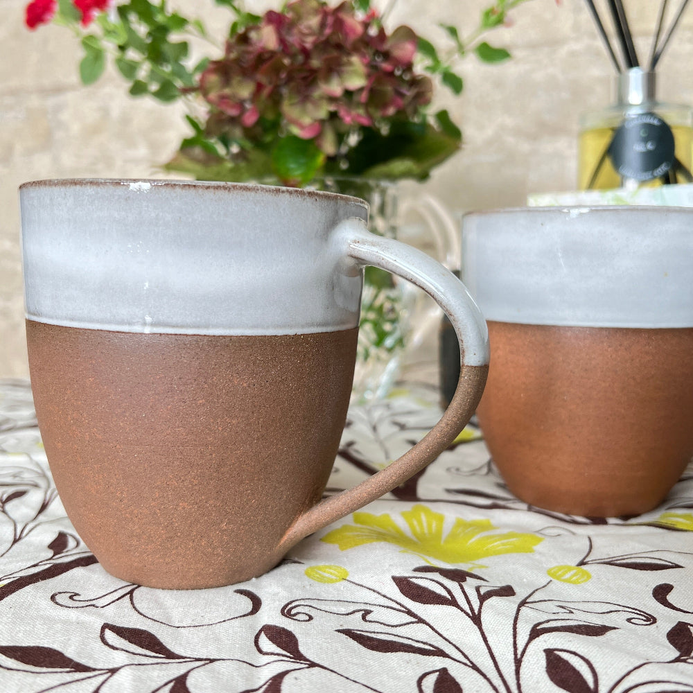 Hand Thrown Mug - Bhaktapur Silk on a patterned tablecloth with a scented room diffuser, fresh flowers and coffee.  Shown against a cotswold stone wall with the Snow Thief book by C J Carver