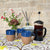 Hand Thrown and Decorated Mug - Bhaktapur Midnight Blue on a table with a Douée tablecloth, coffee, room diffusers and fresh flowers against a cotswold stone wall