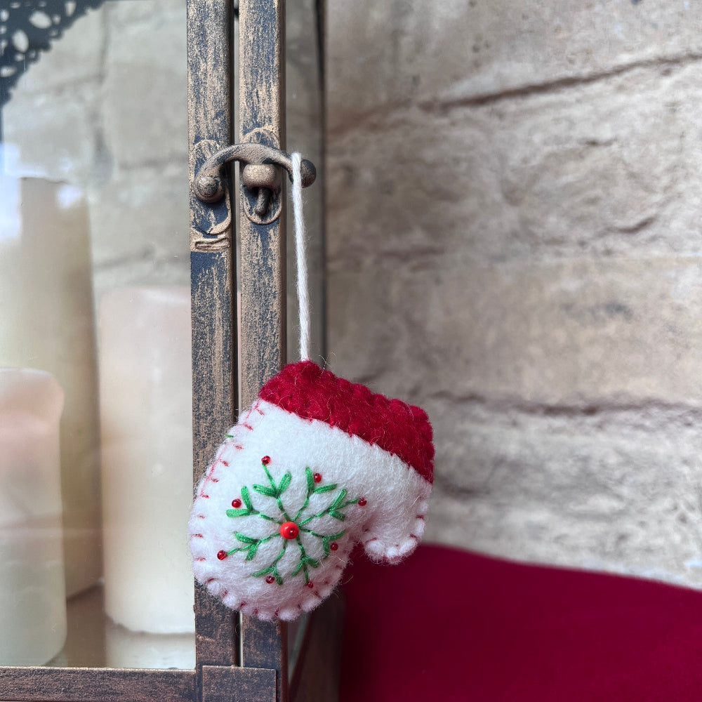Handcrafted Christmas Glove (Mitten) with Embroidered Snowflake and Beaded Decoration against a stone wall backdrop and Seasonal Christmas Candles