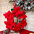 Handcrafted Felted Wool - 'Poinsettia' Wreath with Red Poinsettia Flowers with Green leaves against a stone wool with christmas decor