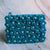 A turquoise pure wool clutch with a daisy pattern, featuring a zipper and a polka and dot and floral design.