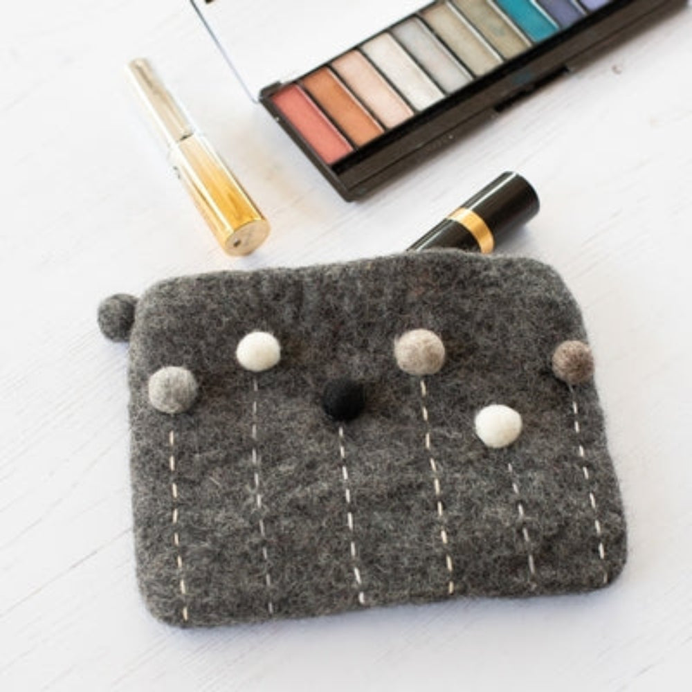 Handcrafted Felted Wool Clutch Bag / Purse with Appliqué Decoration and stitching with makeup o a white background.