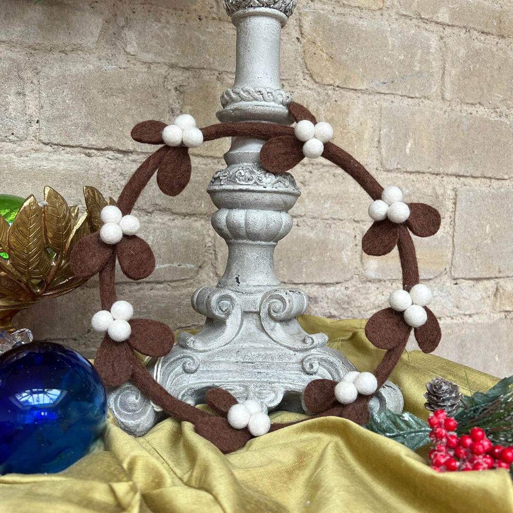 Handcrafted Felted Wool Contemporary Mistletoe Wreath against a stone wool with christmas decorations