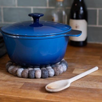 Handcrafted Felted Wool Felted Trivet / Mat - Browns with Grey on a wooden surface with ha blue lidded casserol and a wooden spoon.