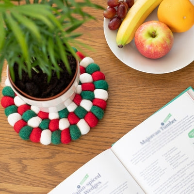 Handcrafted Felted Wool Felted Trivet / Mat - Red, White & Green on a wooden table with fresh fruit and a cookery book