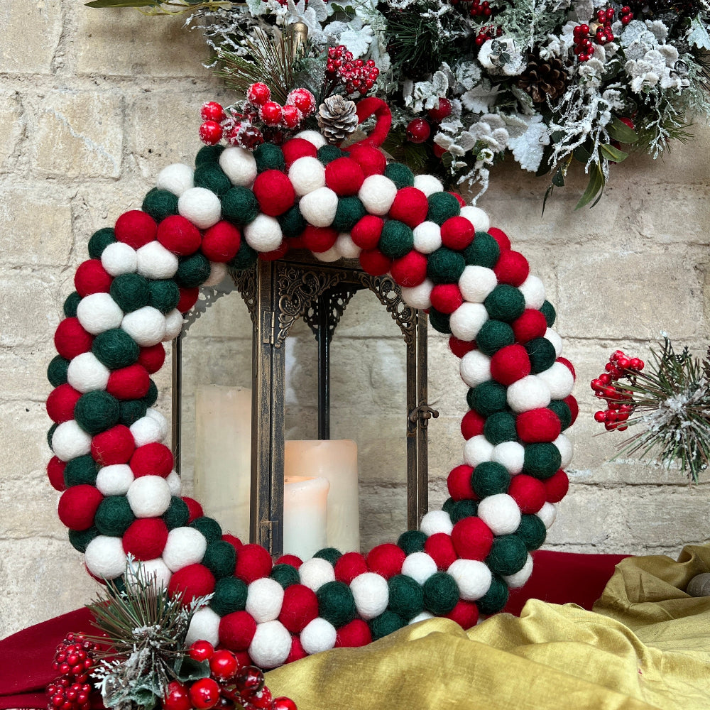 Handcrafted Felted Wool wreath with Red, White & Green colour decoration. A Seasonal Wreath against a stone wall with Christmas decorations and candles.