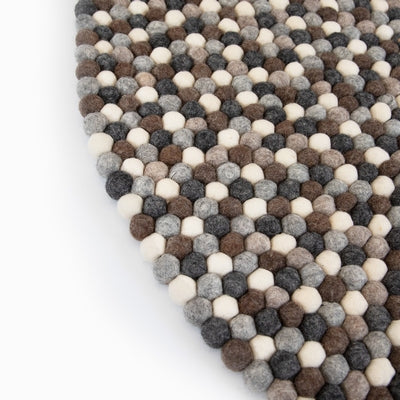Handcrafted Felted Wool Rugs - Assorted  Browns, Grey and Cream available by Douée on a natural colour carpet in a room with tables and a natural colour sofa against a neutral wall with a green plant for decoration. 