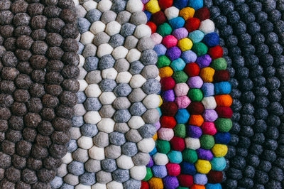 Handcrafted Felted Wool Rugs - Multi-coloured by Douée, on a natural colour carpet in a room with tables and a natural colour sofa. 