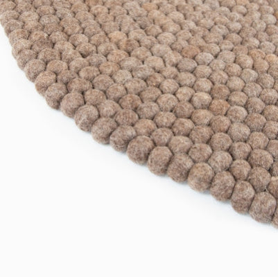 Handcrafted Felted Wool Rugs - Chocolate Brown available by Douée on a natural colour carpet in a room with tables and a natural colour sofa against a neutral wall with a green plant for decoration. 