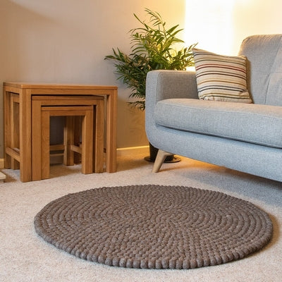 Handcrafted Felted Wool Rugs - Chocolate Brown available by Douée on a natural colour carpet in a room with tables and a natural colour sofa against a neutral wall with a green plant for decoration. 