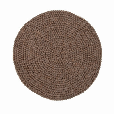Handcrafted Felted Wool Rugs - Chocolate Brown available by Douée on a natural colour carpet in a room with tables and a natural colour sofa against a neutral wall with a green plant for decoration. 