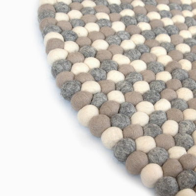 Handcrafted Felted Wool Rugs - Cream, Browns and Grey by Douée on a natural colour carpet in a room with tables and a natural colour sofa against a neutral wall with a green plant for decoration. 