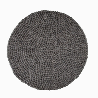 Handcrafted Felted Wool Rugs - Grey by Douée on a natural colour carpet in a room with tables and a natural colour sofa against a neutral wall with a green plant for decoration. 