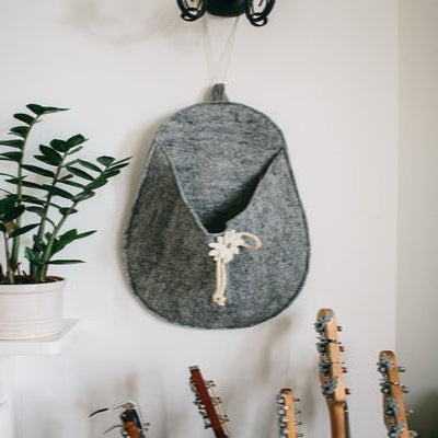 A gray felted wool storage slipper with a floral applique and a wooden button, hanging on a wall.