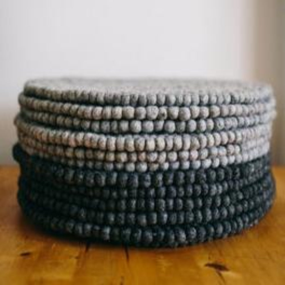 A stack of dark grey and grey pure wool table mats, handcrafted, hand-knotted and hand-sewn, displayed on a wooden surface.