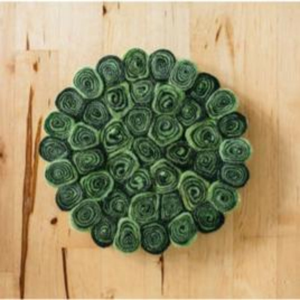 A round green and black trivet stand made of felted wool crafted by hand on a wooden table.
