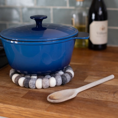 Handcrafted Felted Wool Trivet / Mat - Browns, Grey and Cream with a blue lidded casserol, wooden spoon on a wooden work surface.