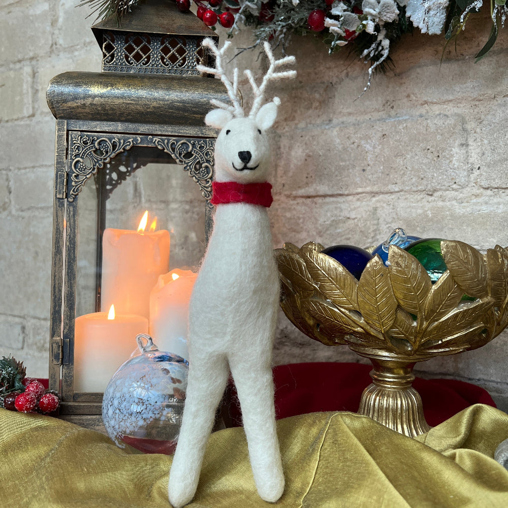 Handcrafted Felted Wool Winter Reindeer with Red Scarf against a stone wall with Candlestick and Christmas Decorations