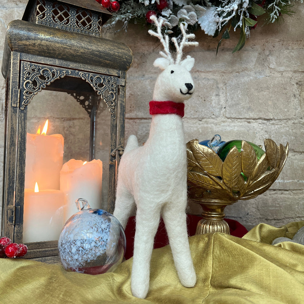 Handcrafted Felted Wool Winter Reindeer with Red Scarf against a stone wall with Candlestick and Christmas Decorations