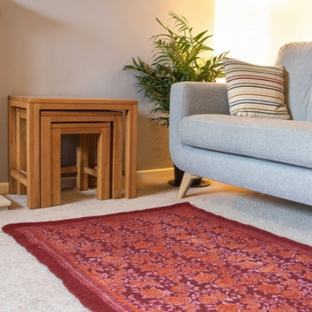 A rectangular, burgundy-colored felted wool rug with a floral pattern, placed on a gray sofa in a living room setting.