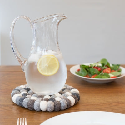 Handcrafted Felted Wool Trivet / Mat - Browns, Grey and Cream with a blue lidded casserol, wooden spoon on a wooden work surface.