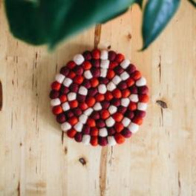 This handcrafted felted wool trivet combines vibrant multicoloured design with durable, sustainable materials.

Its hardwearing construction offers reliable protection for your surfaces while adding an elegant bright touch of colour to your home.

Shown on a white table with a green leafed plant. 